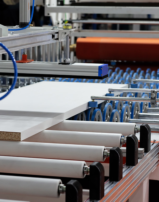 Industrial machinery with a white panel moving on rollers during processing.
