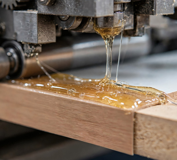 Hot-melt adhesive being applied from a machine onto a wooden surface.